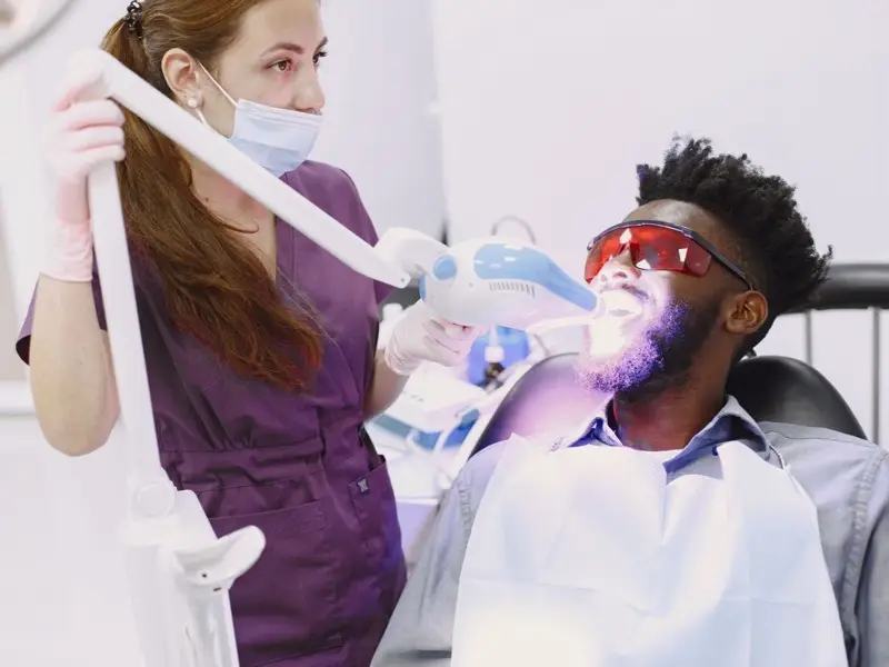 A patient receiving an in-clinic whitening treatment under a blue lamp