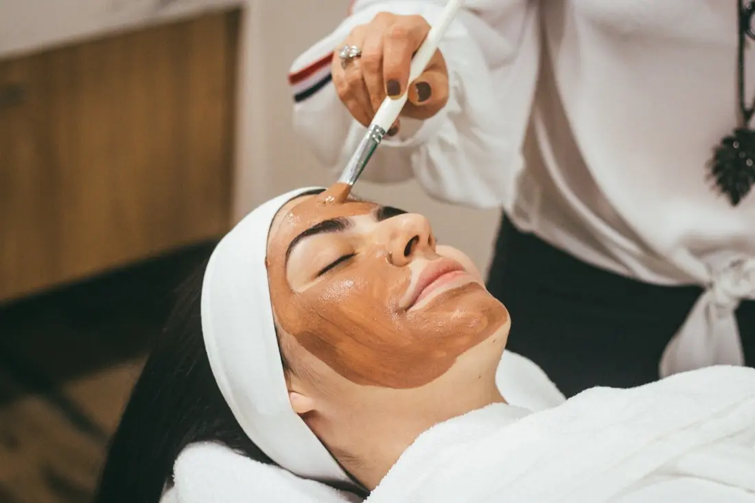 A facial treatment in progress: a therapist applying a mask with a brush while the client rests