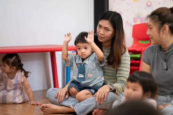 A teacher and a toddler with their hands raised, playing a game